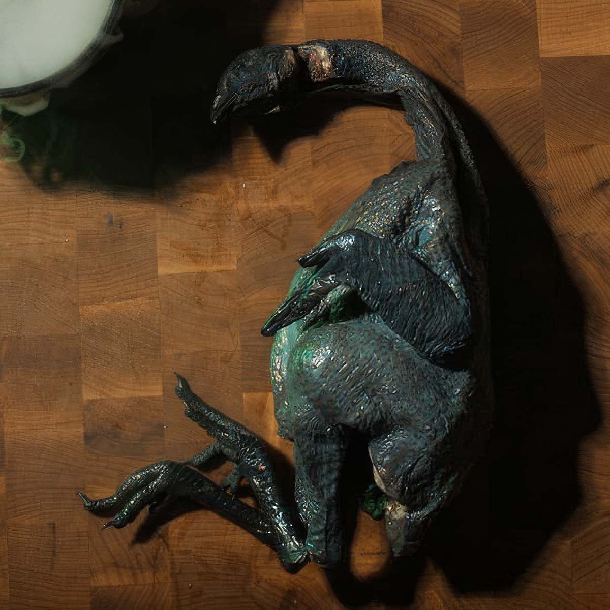 A whole jet black silkie chicken rests on a cutting board. It resembles a baby dragon.