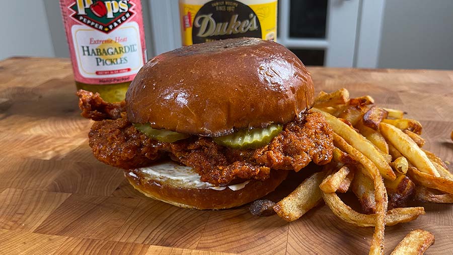 Nashville Hot Chicken Sandwich on a cutting board with French fires.