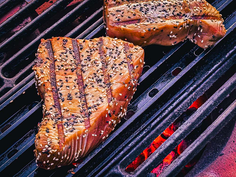 Grilled Tuna Steak sizzles on a cast iron grate over charcoal