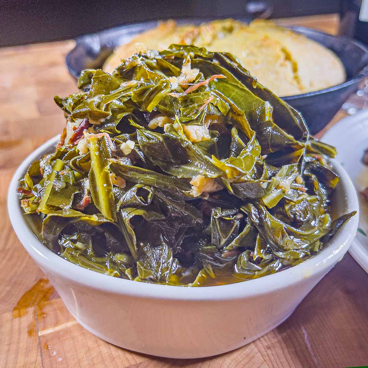 Warm bowl of southern style collard greens rests on a cutting board.