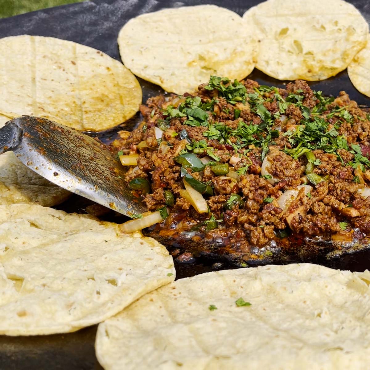 Tortillas line a discada with meat sizzling in the middle.