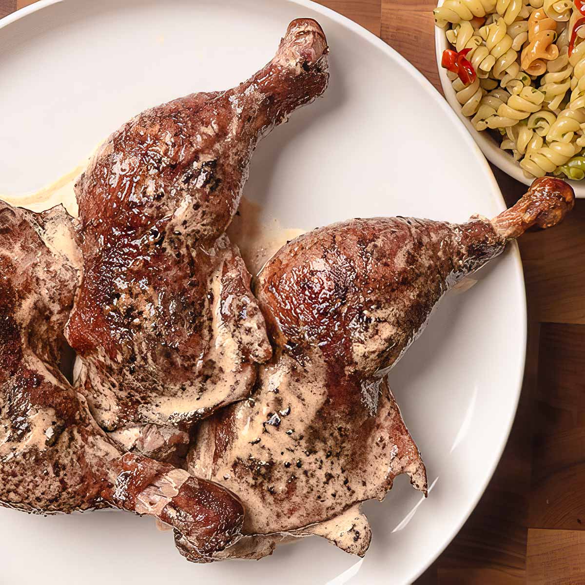 Smoked Chicken Leg Quarters dripping with Alabama White Sauce sit on a plate next to a small bowl of pasta salad.