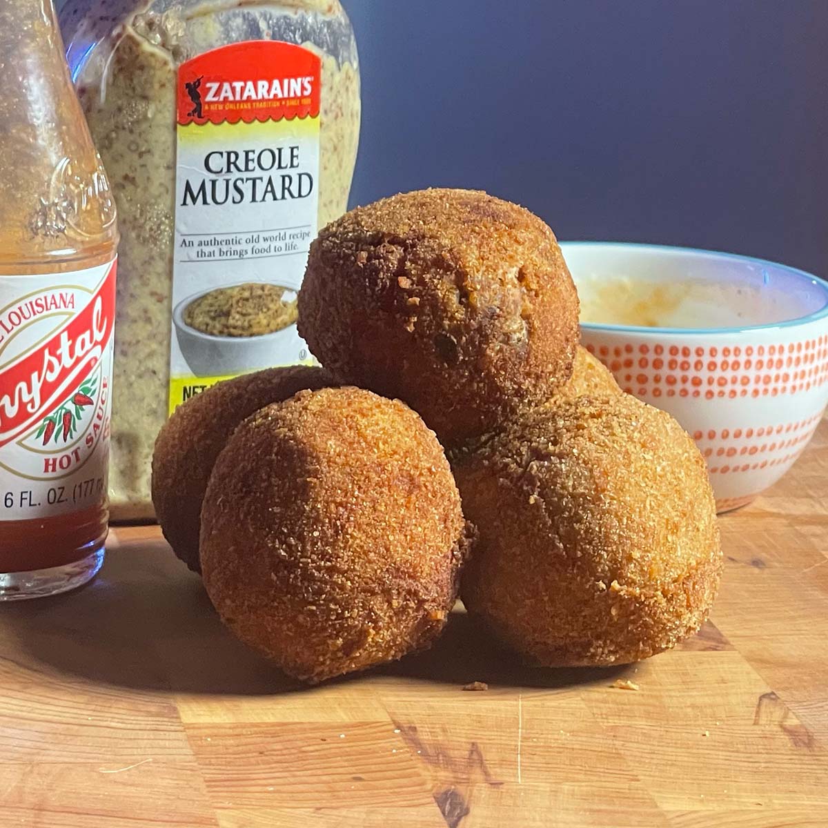Golden brown boudin balls rest on a cutting board flanked by hot sauce and creole mustard.