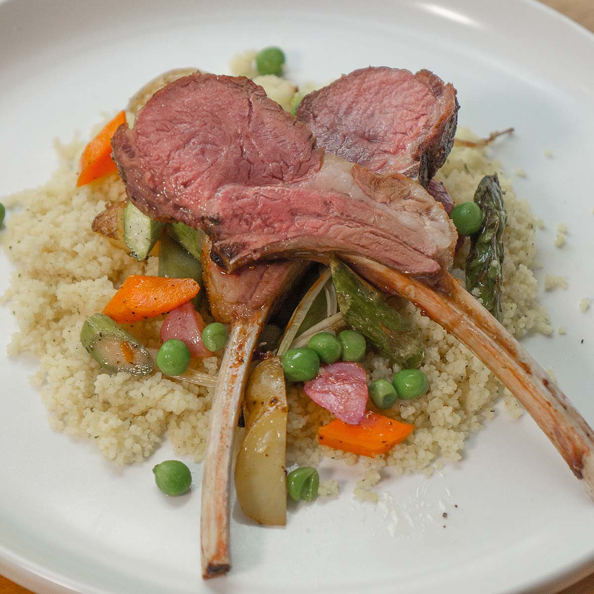 Grilled lamb chops rest on a bed of spring vegetables and couscous.