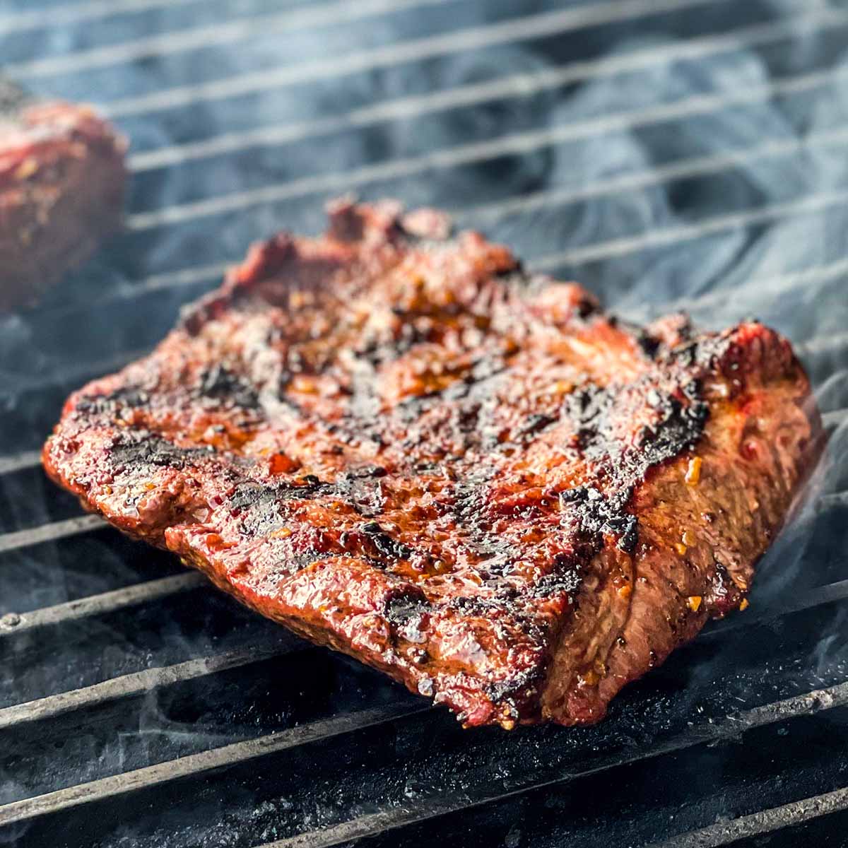 A juicy steak is seared on a grill as smoke wafts into the air.
